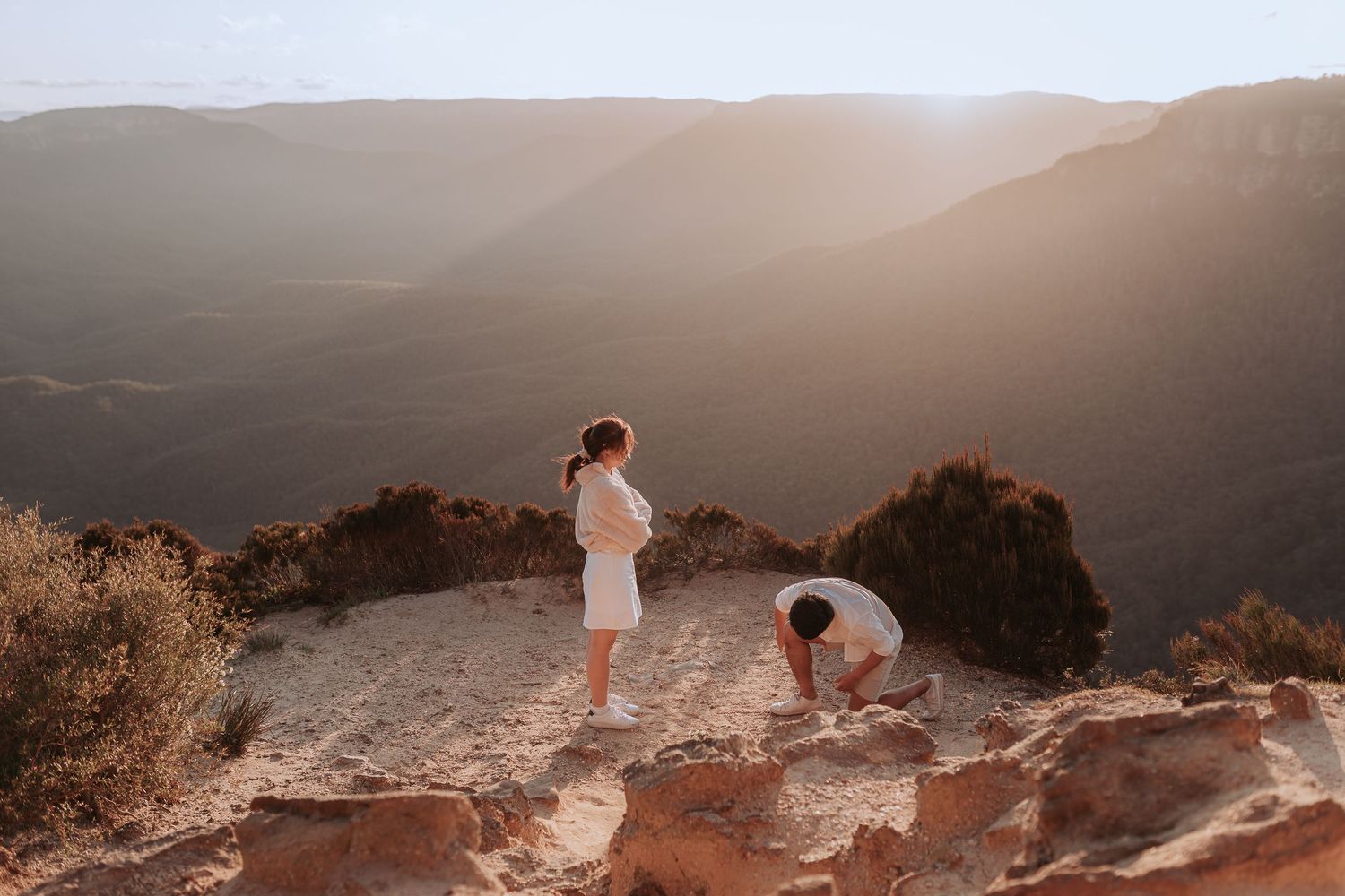 A couple sharing a moment on a rocky mountain overlook at sunset.