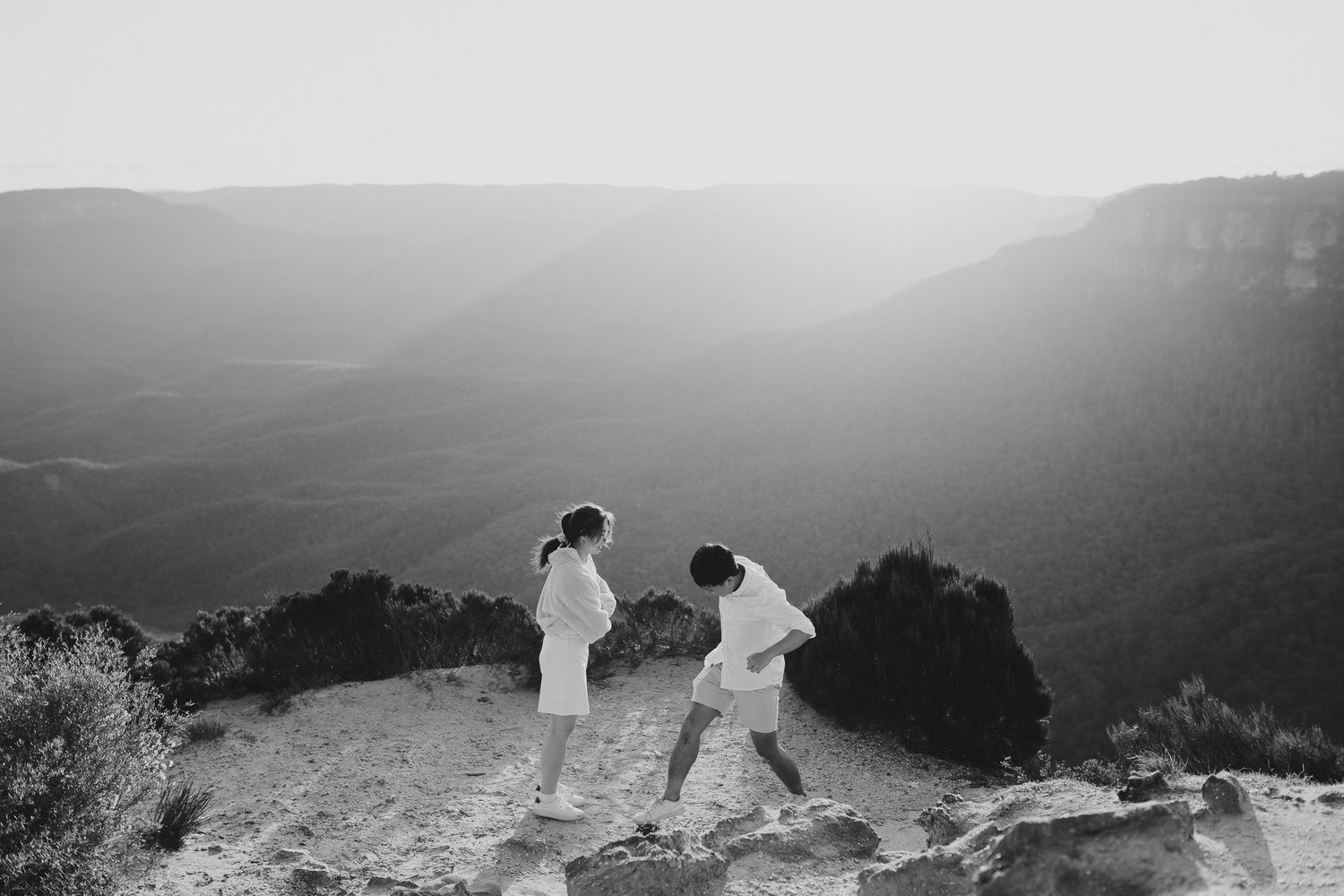 Couple in white outfits dancing together on a mountain overlook during sunset.