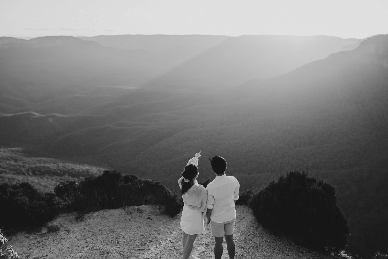 Two people in white outfits admiring a scenic mountain valley view.