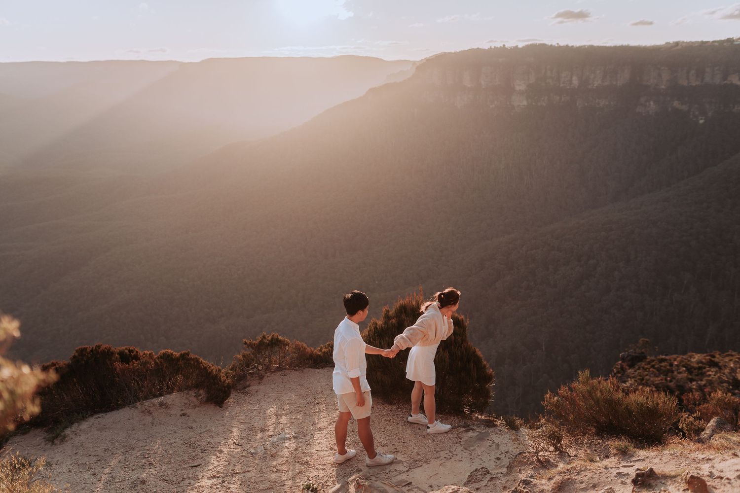 Three people enjoying a scenic mountain overlook at sunset.