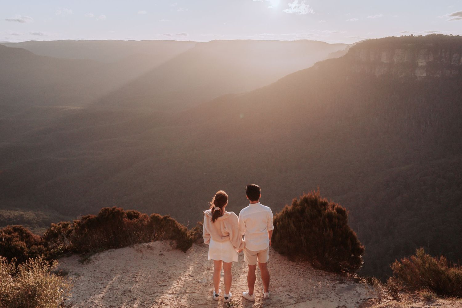 Couple in matching white outfits admiring a sunset mountain vista together.