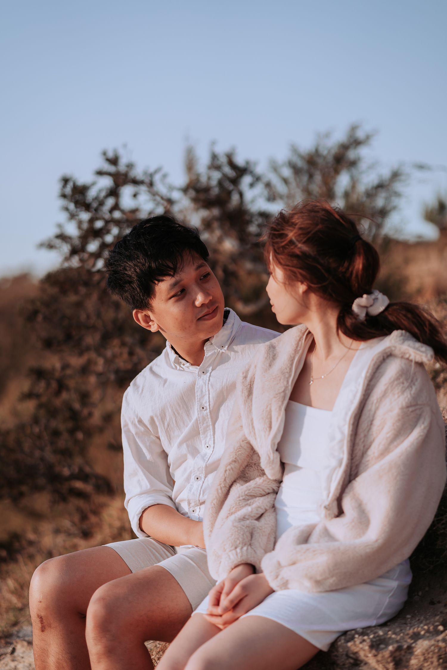 Romantic couple sitting together on rocky terrain with desert plants in background.