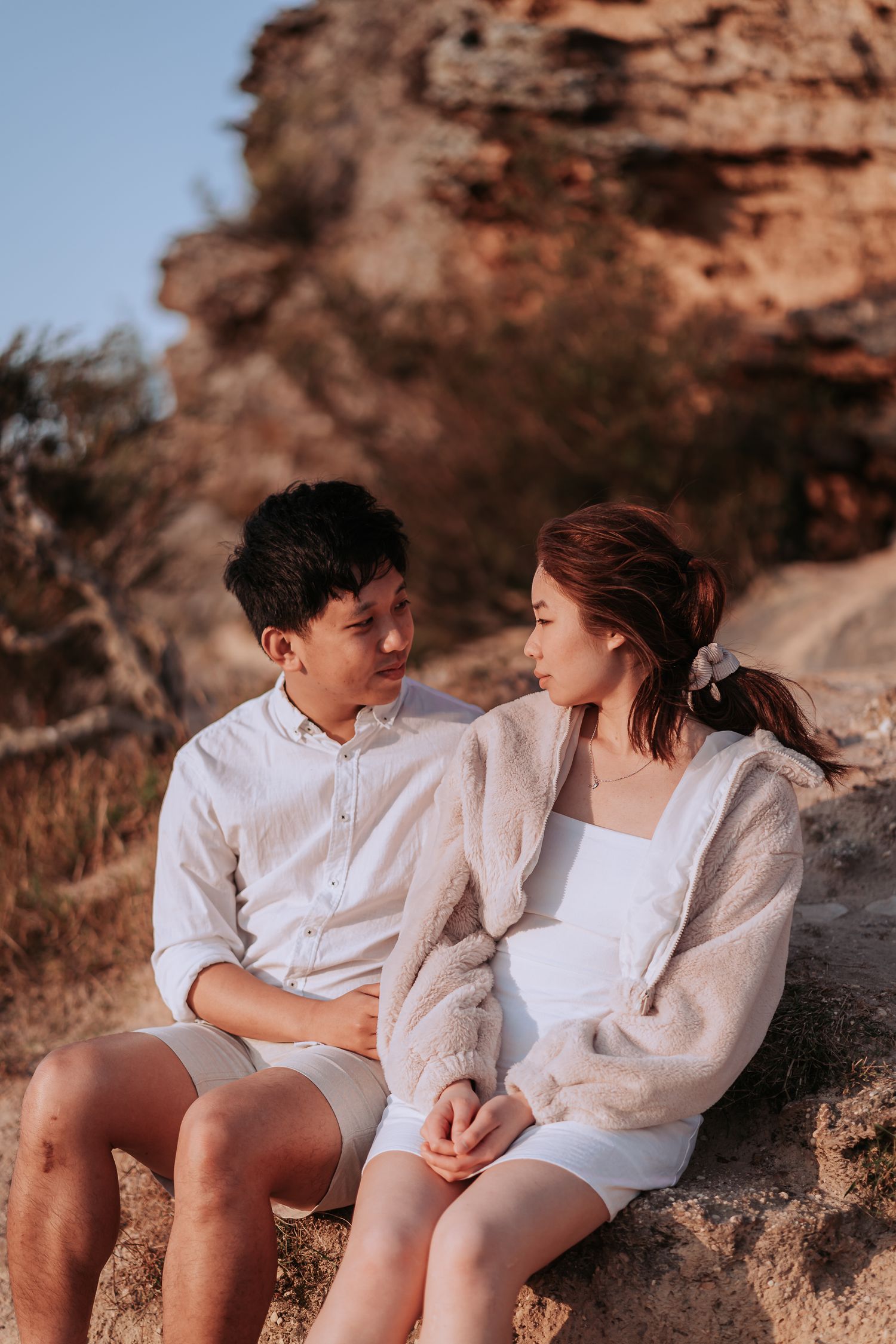 Couple sharing an intimate moment while sitting on rocky outcrop during sunset.