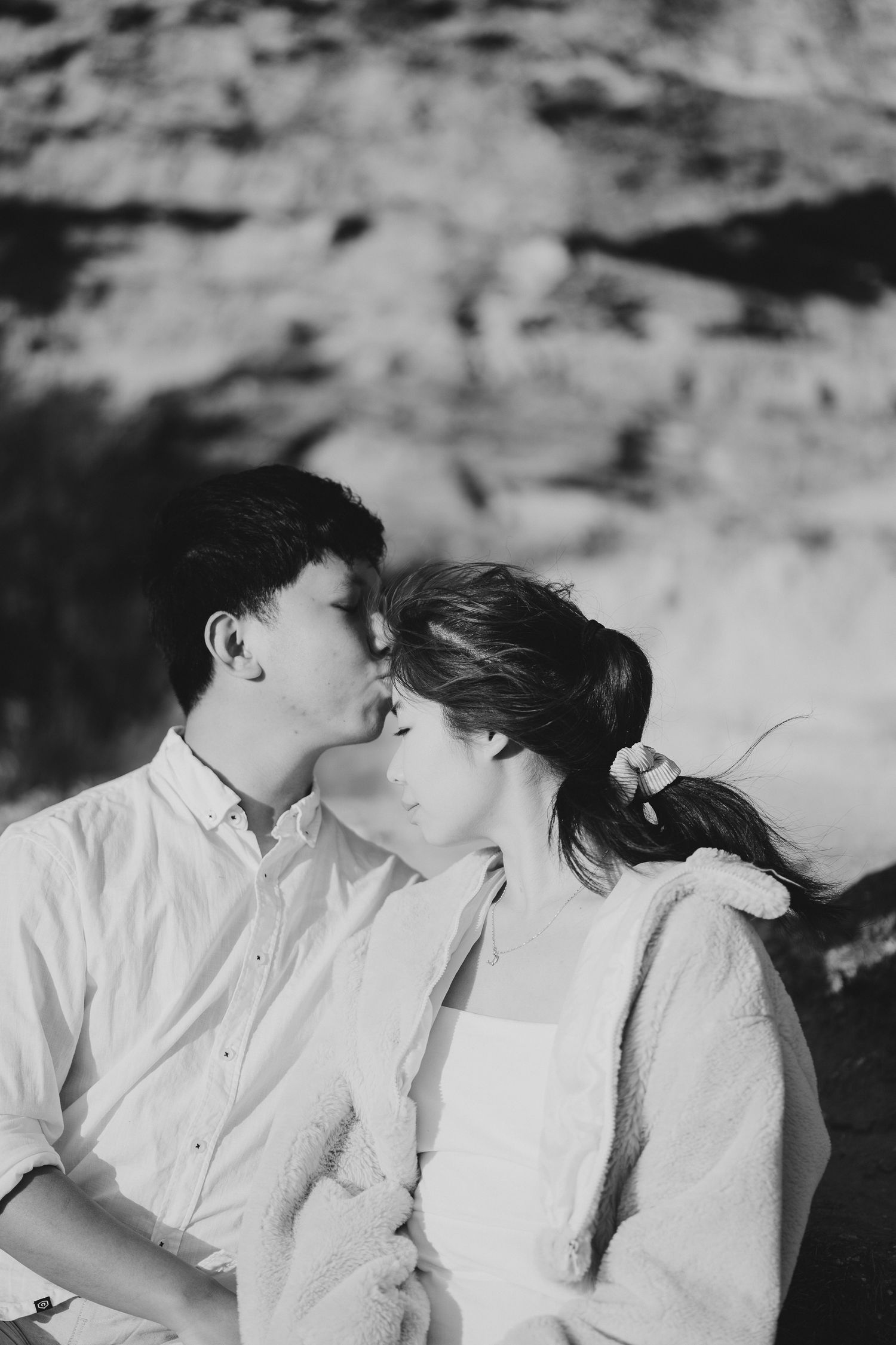 An intimate black and white portrait of a couple sharing a tender moment against rocky backdrop.