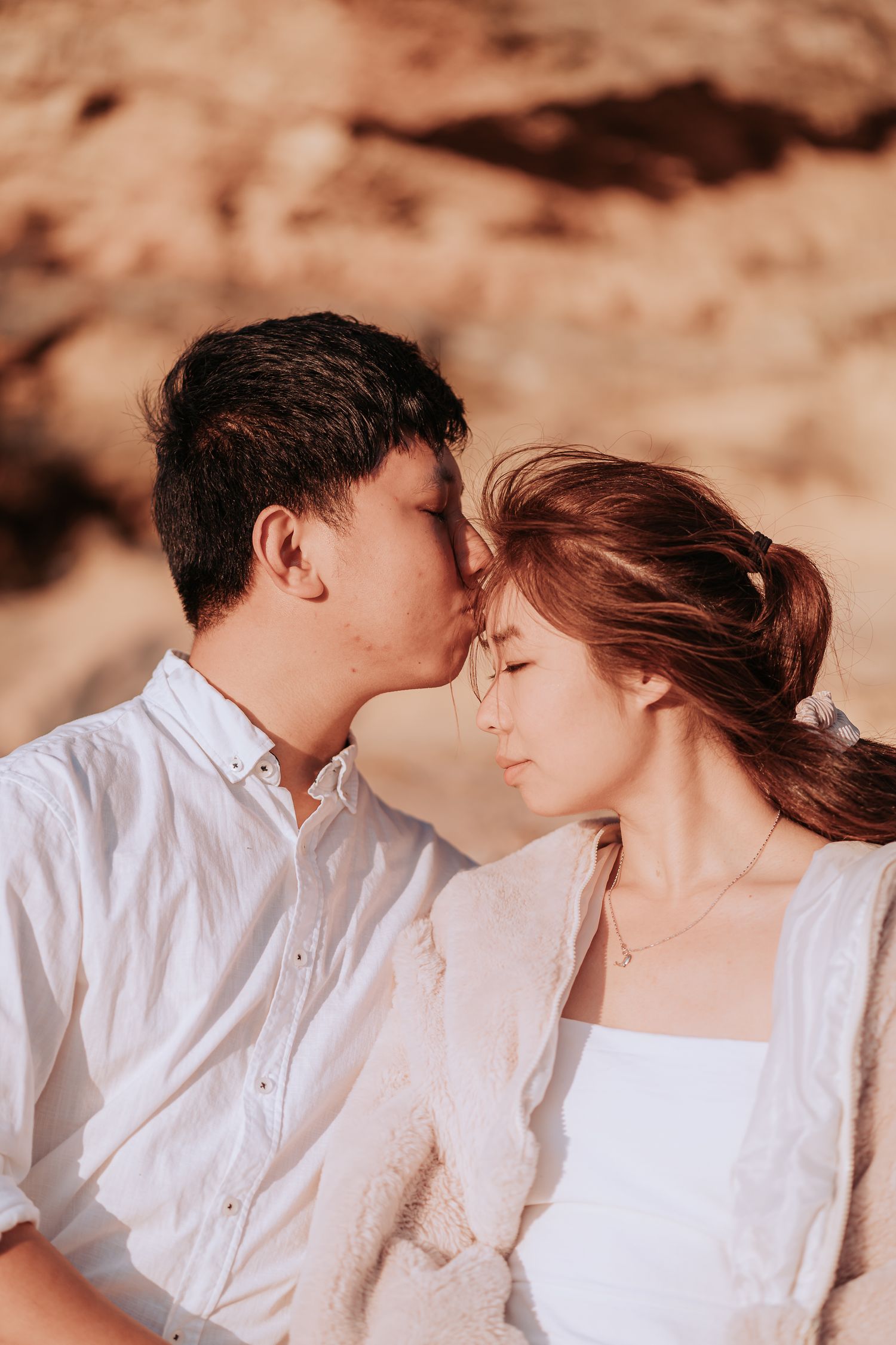 A tender moment between a couple wearing white against a sunlit rocky backdrop.