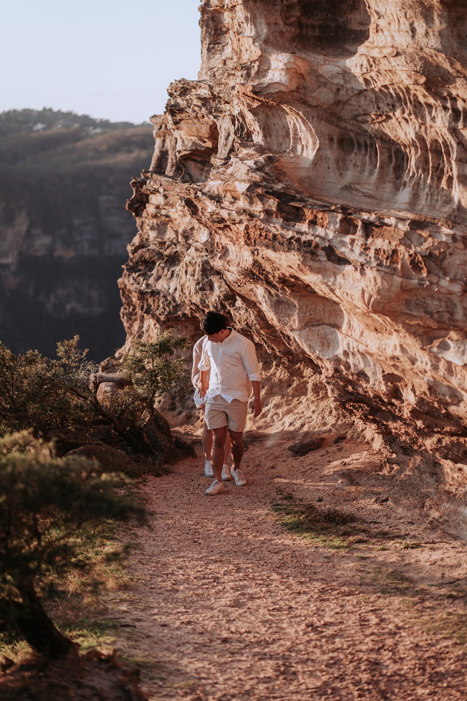 A person in white clothing walks along a scenic mountain trail during golden hour.