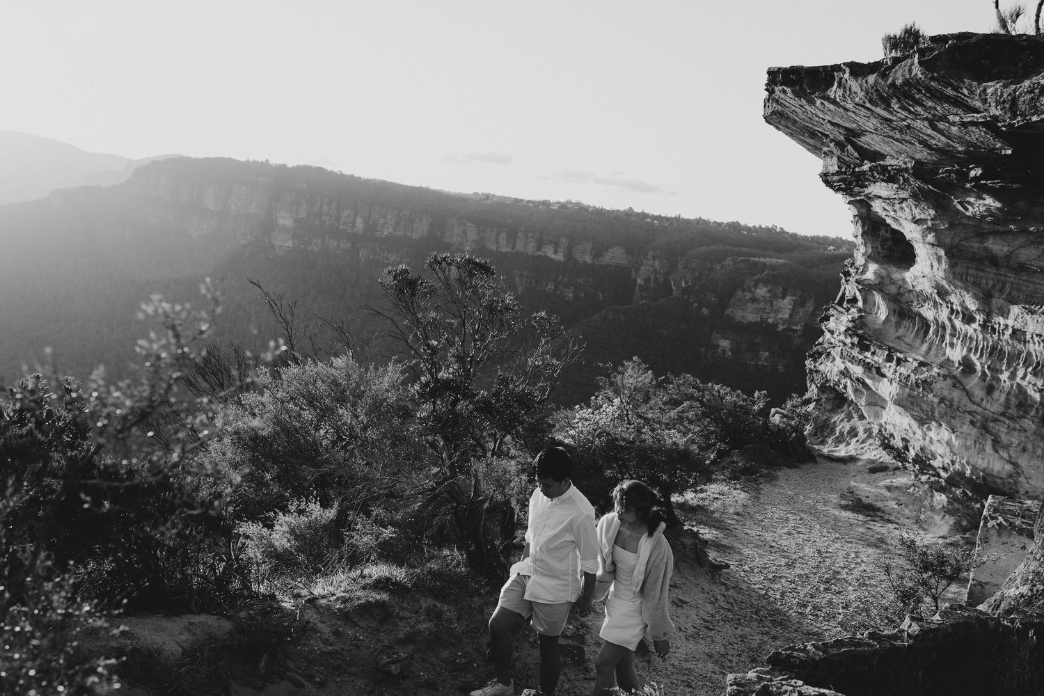 A black and white landscape photo of two people walking along a mountain path.