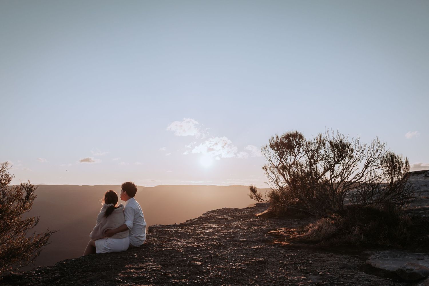 Two lovers share an intimate moment watching the sun set over mountain peaks.