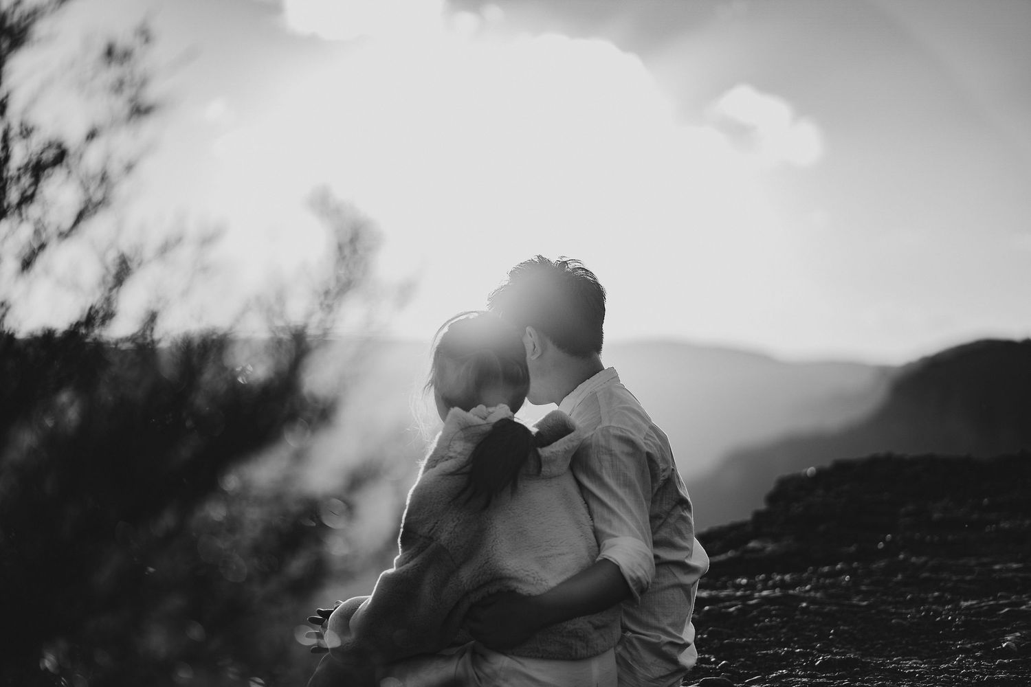 A person in white clothing sits thoughtfully on a mountain edge during golden hour.