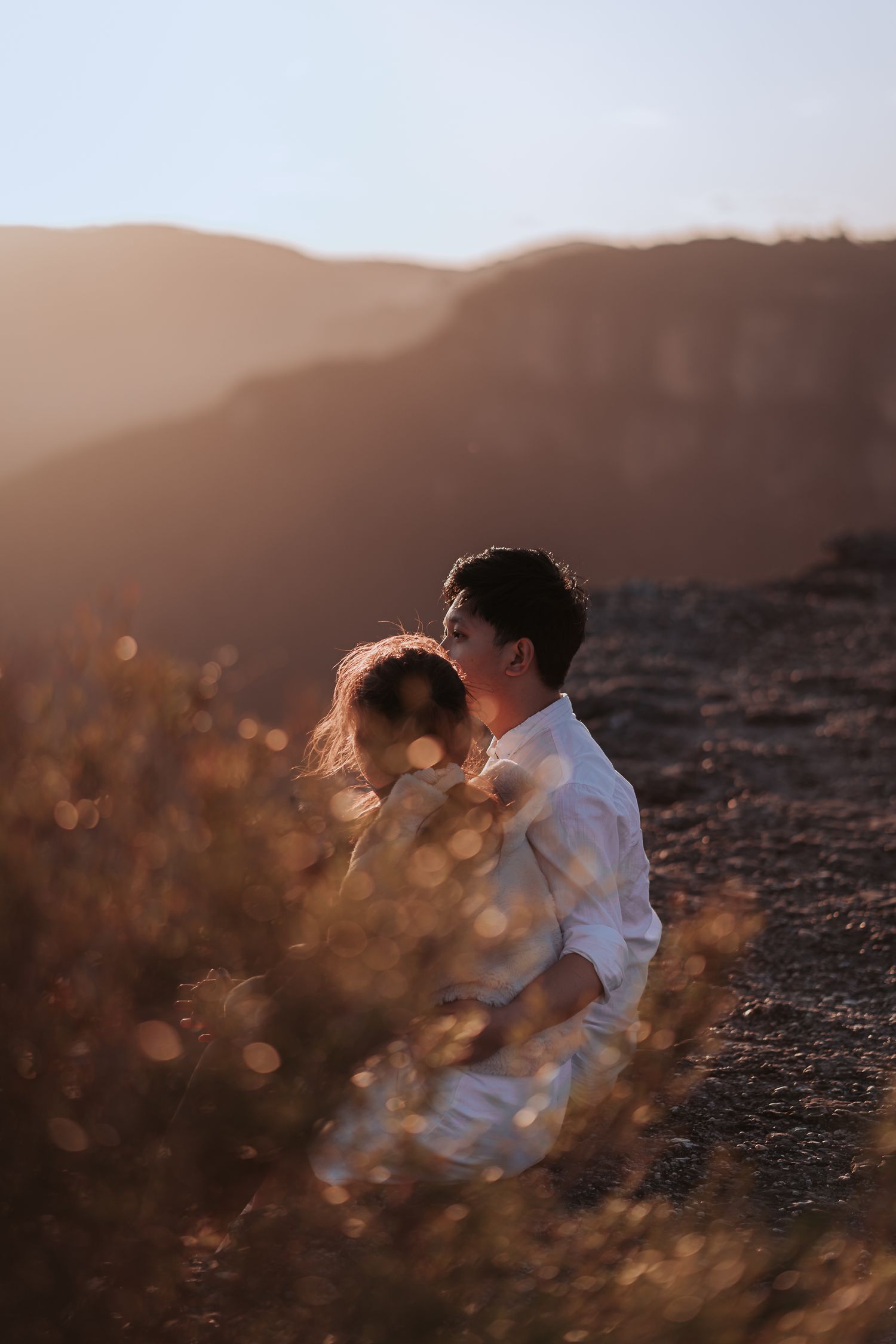 A couple sharing a tender moment in golden sunlight with mountains in the background.