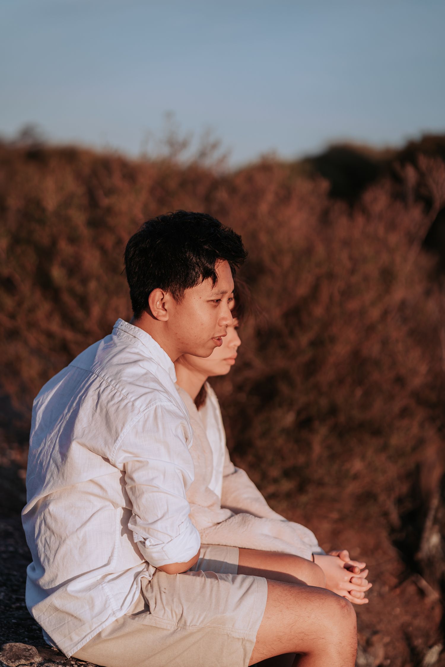 A person in white shirt sits contemplatively on rocky terrain at sunset.