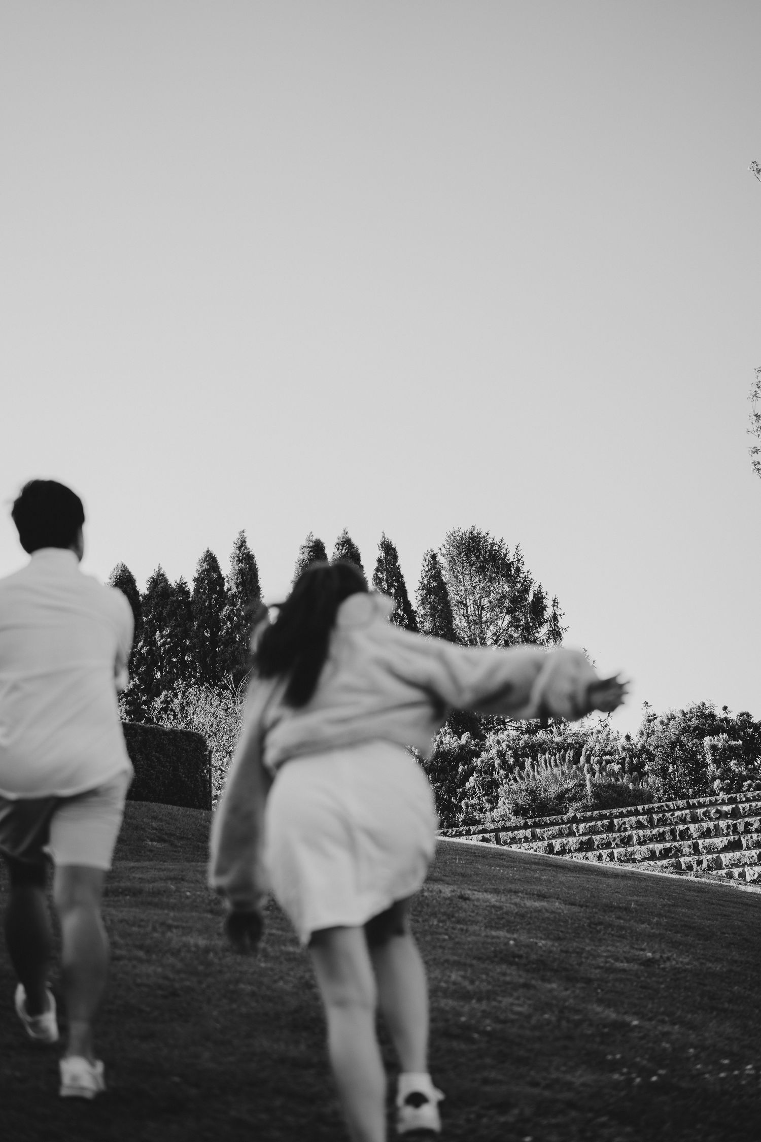 Two figures running up a grassy hill against a grey sky with trees in the background.