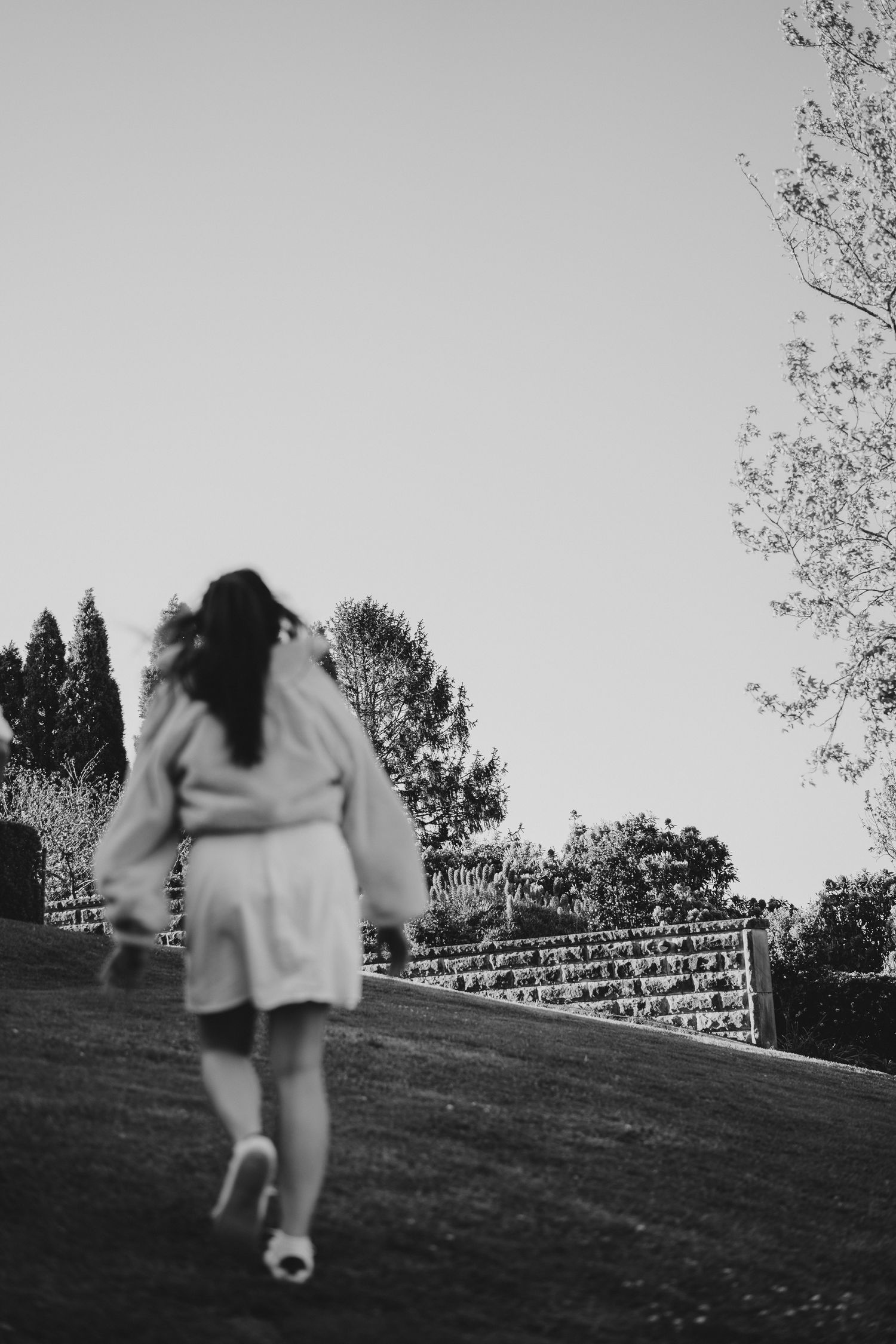 A person in white clothing running up a grassy hill with evergreen trees in the background.