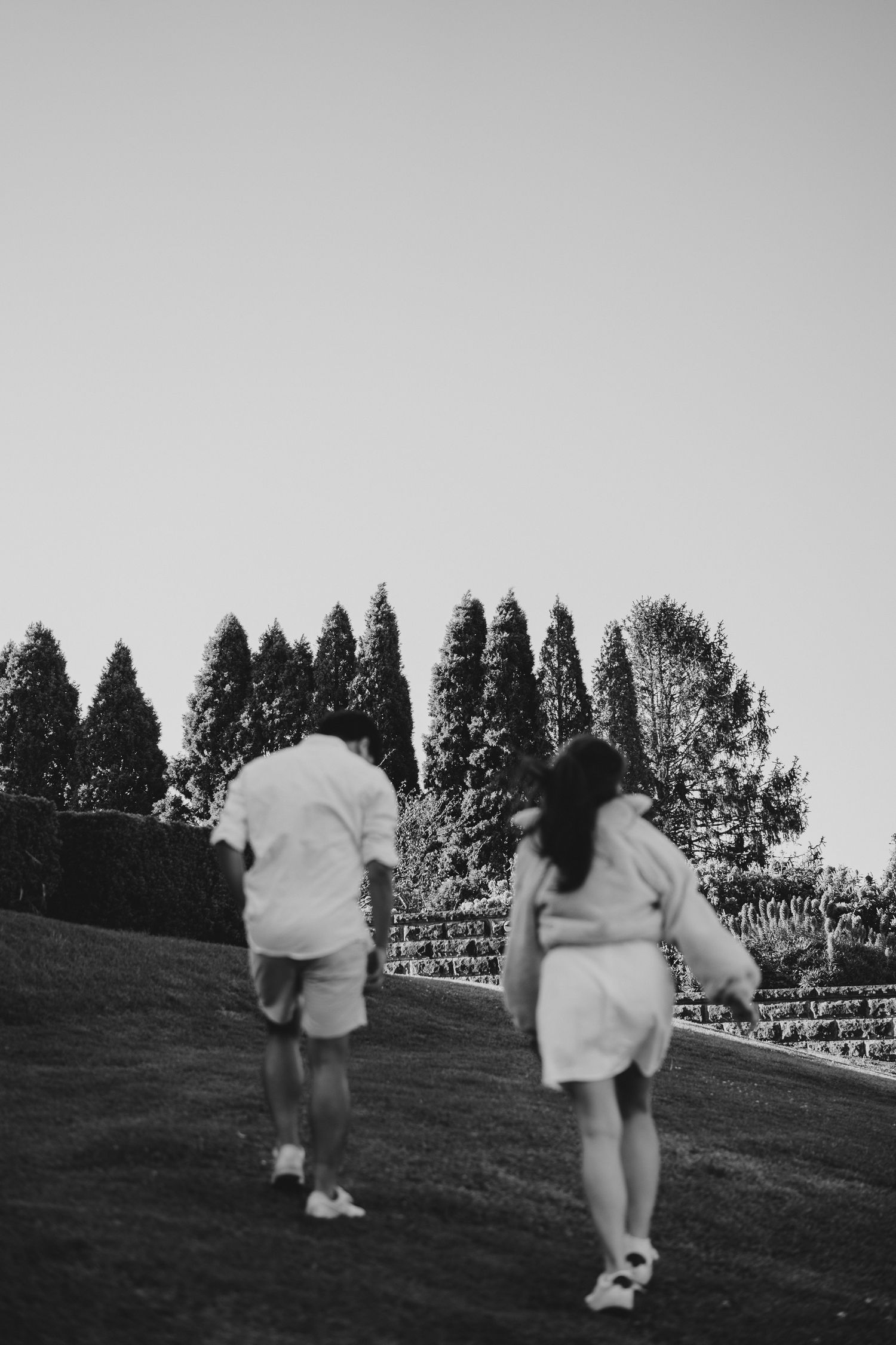 Two people running uphill together wearing matching white outfits on a grassy slope.