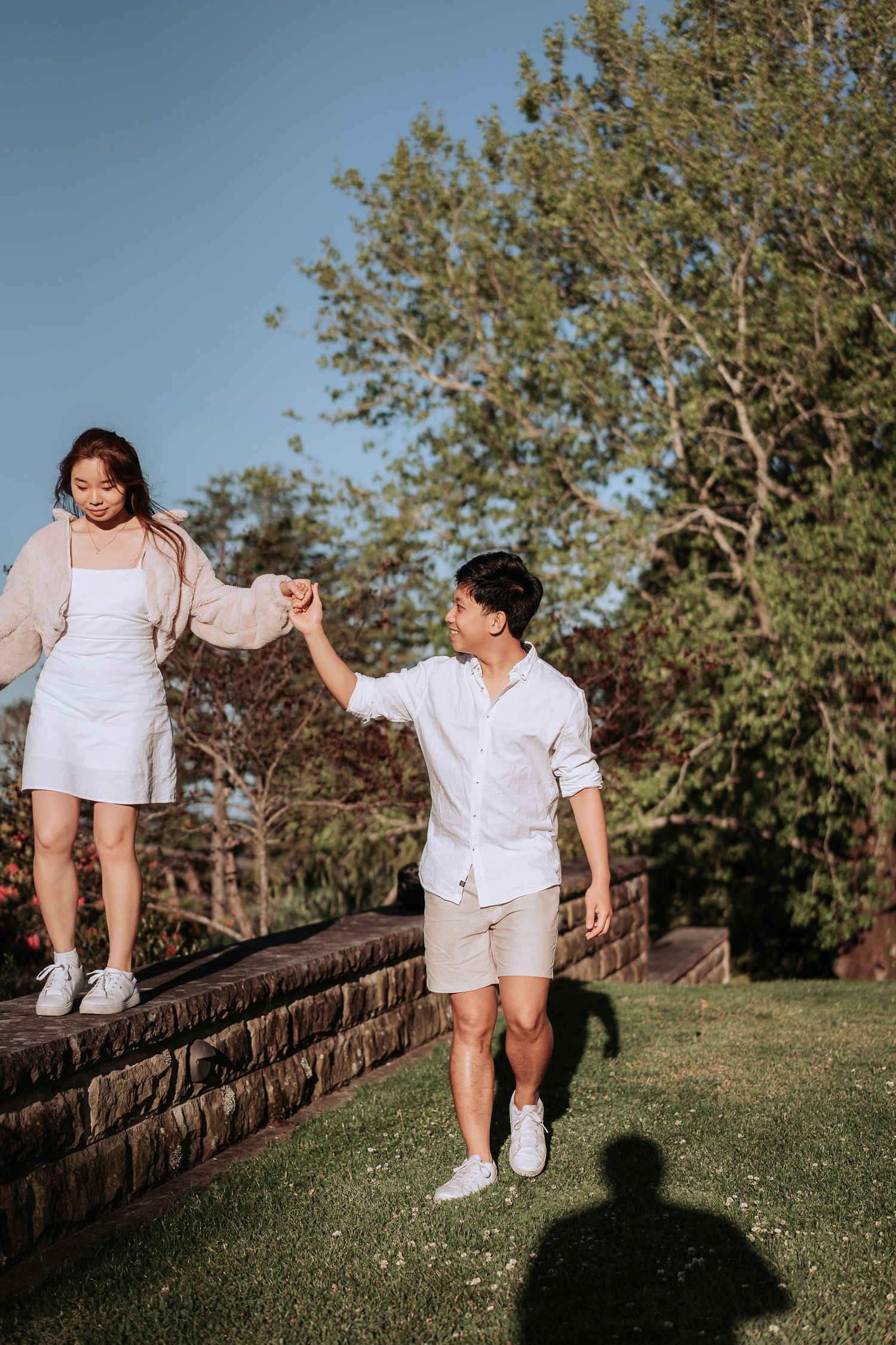 A couple in coordinated white outfits share a playful moment on stone steps in a garden.