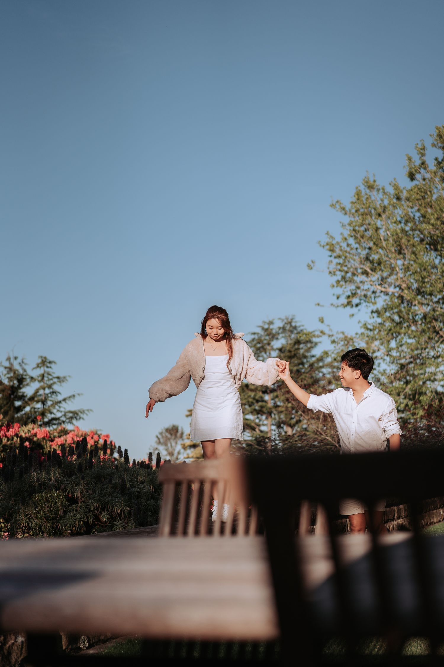 A couple balancing on a garden wall surrounded by spring flowers and trees.