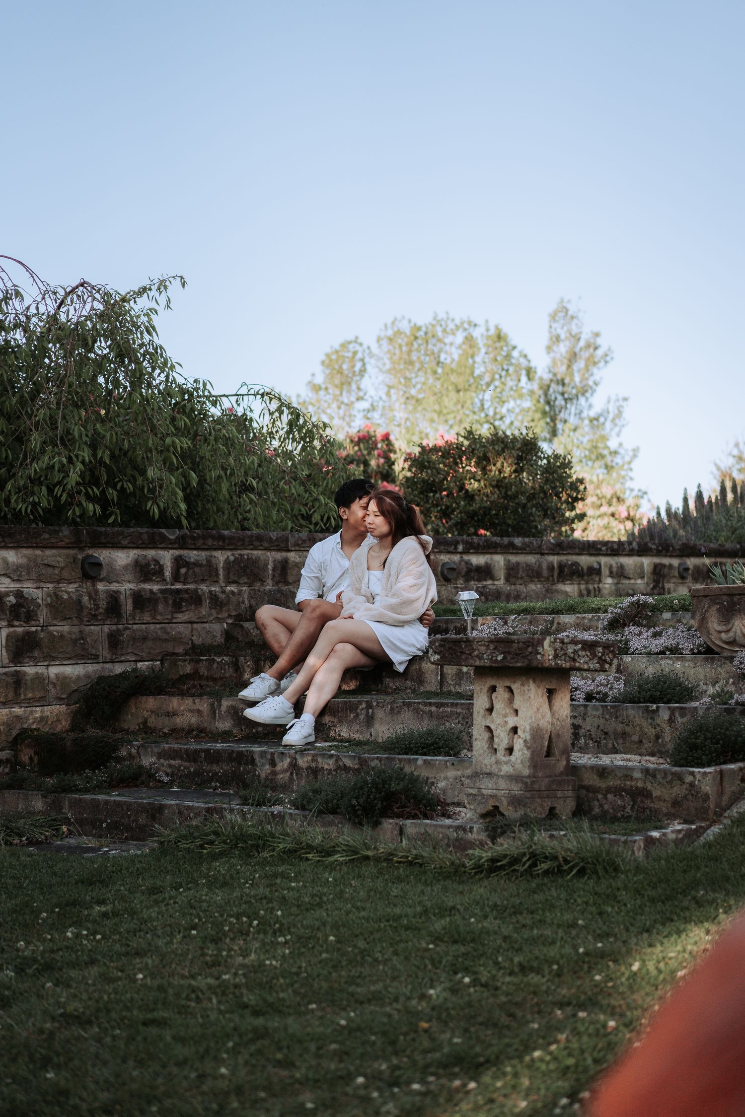 A romantic couple sits close together on rustic stone steps during golden hour.
