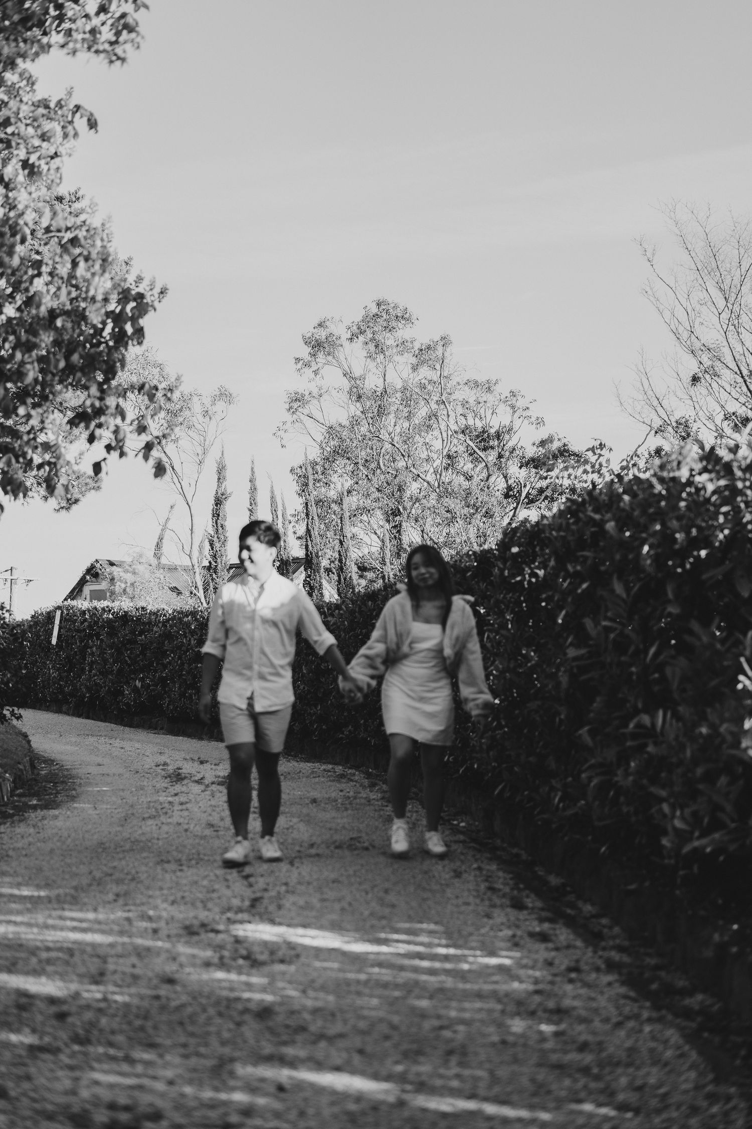 A monochrome image of two people strolling hand in hand down a hedged garden pathway.