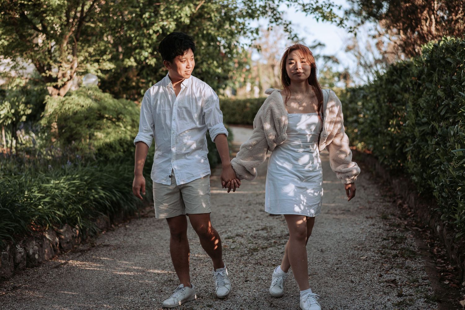 A couple walks together on a dirt trail wearing coordinated white outfits and sneakers.