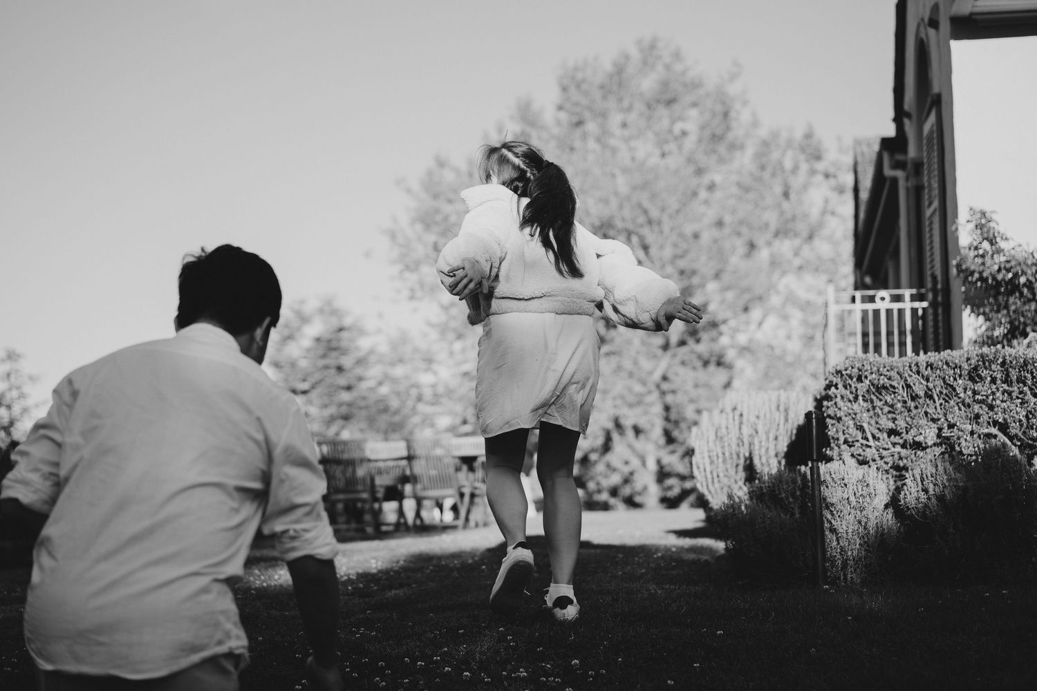 A black and white capture of a person dancing while another sits on a garden terrace.