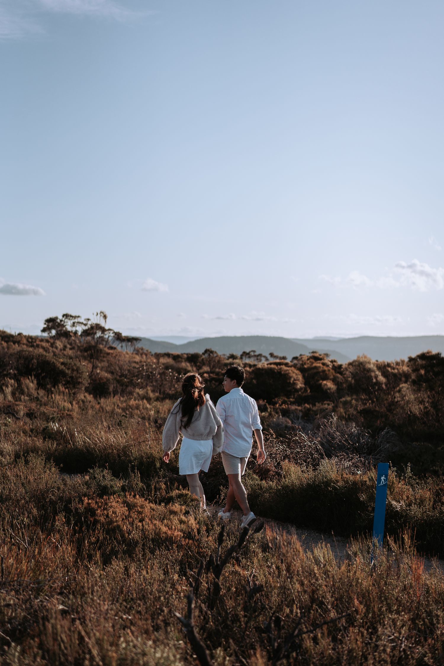 Two people in white outfits explore a scenic hilltop trail during golden hour.