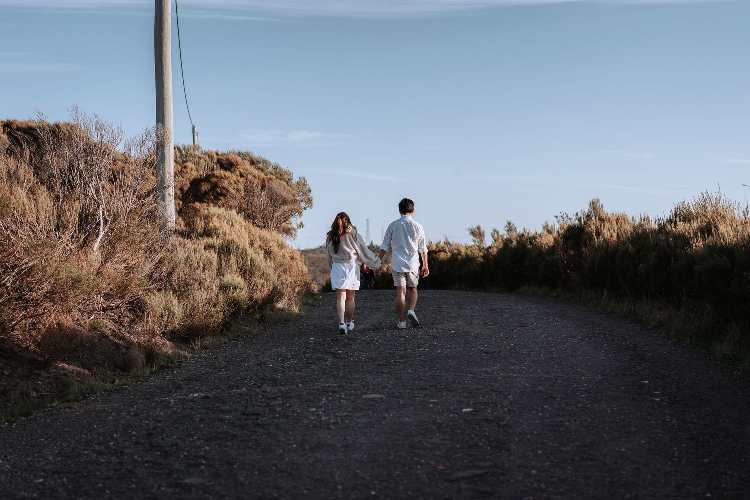 Two people walk along a dark path with mountains in the distance.