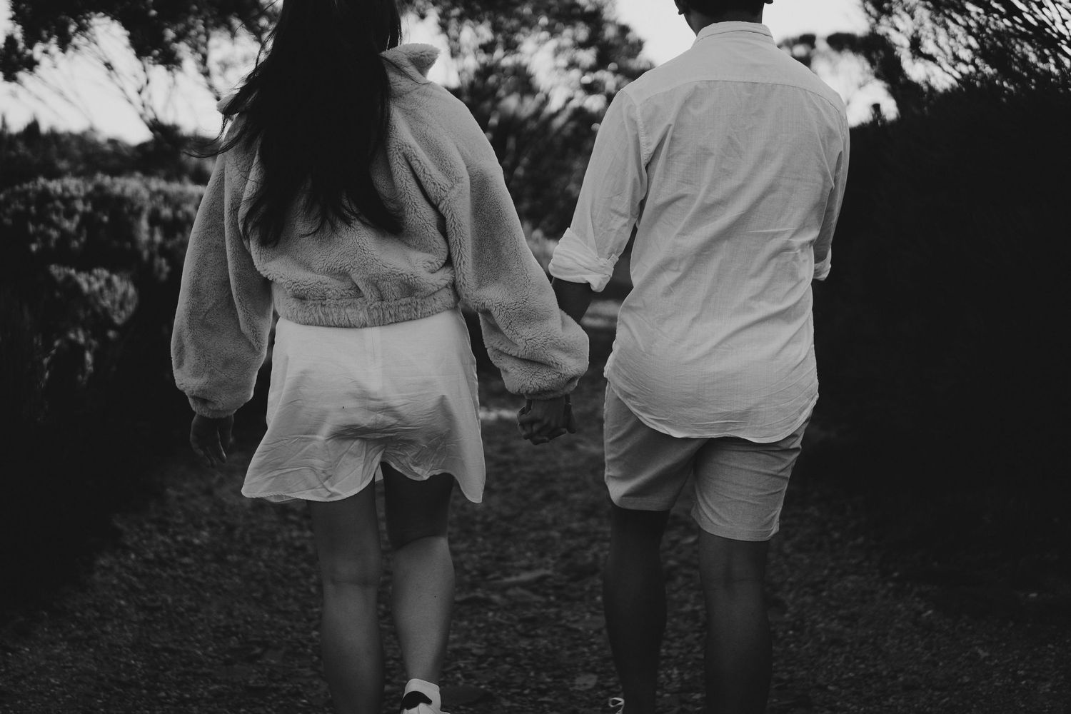 Black and white photo of two people walking together on a path through trees.