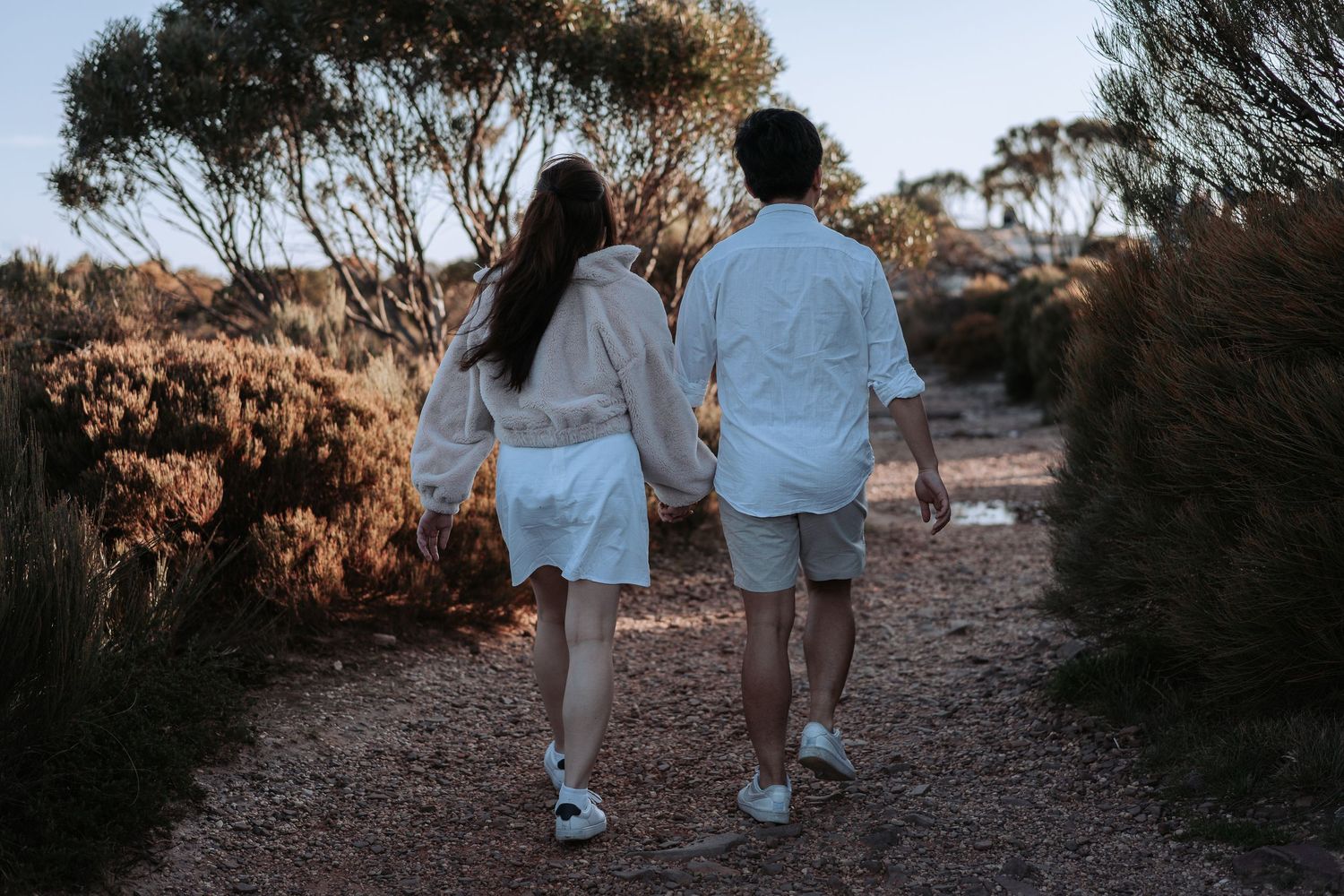 Two people in matching white outfits walking hand in hand on a rustic hiking trail.