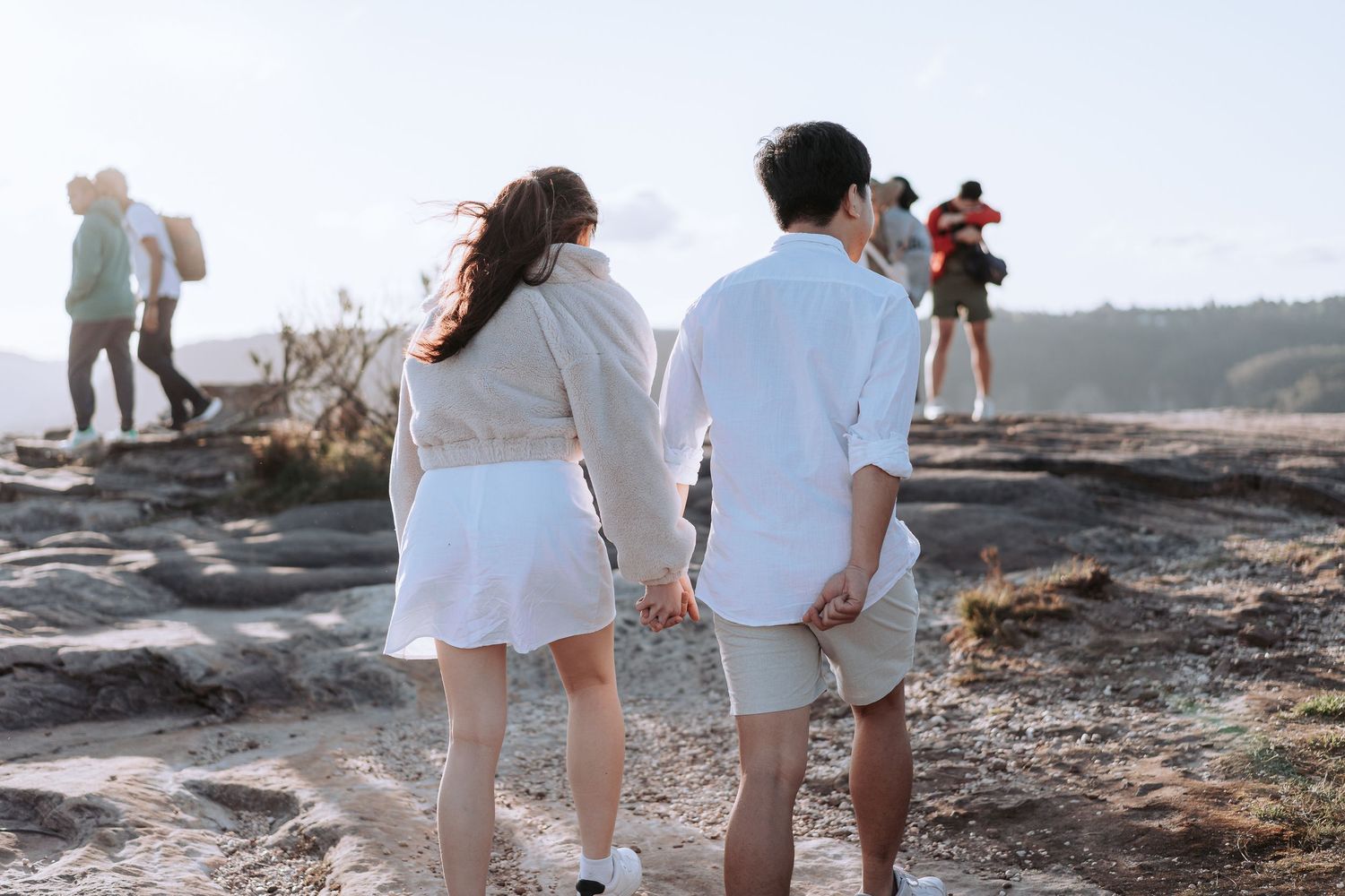 People in white clothing walking on rocky terrain with other hikers visible in background.