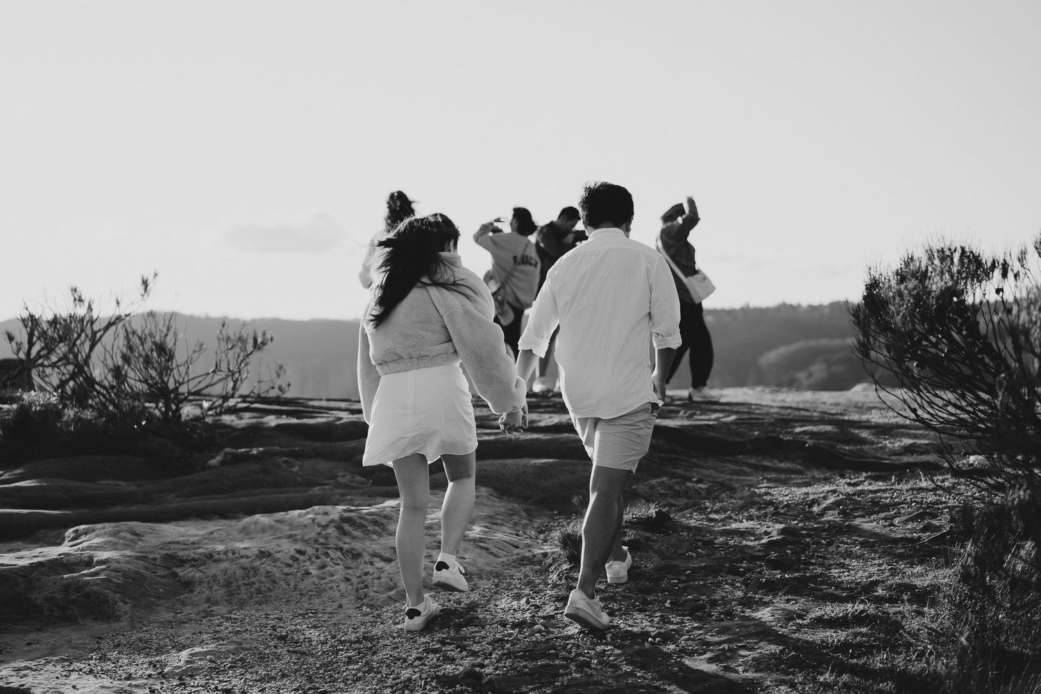 A black and white photo of people walking on a rugged mountain path during sunset.
