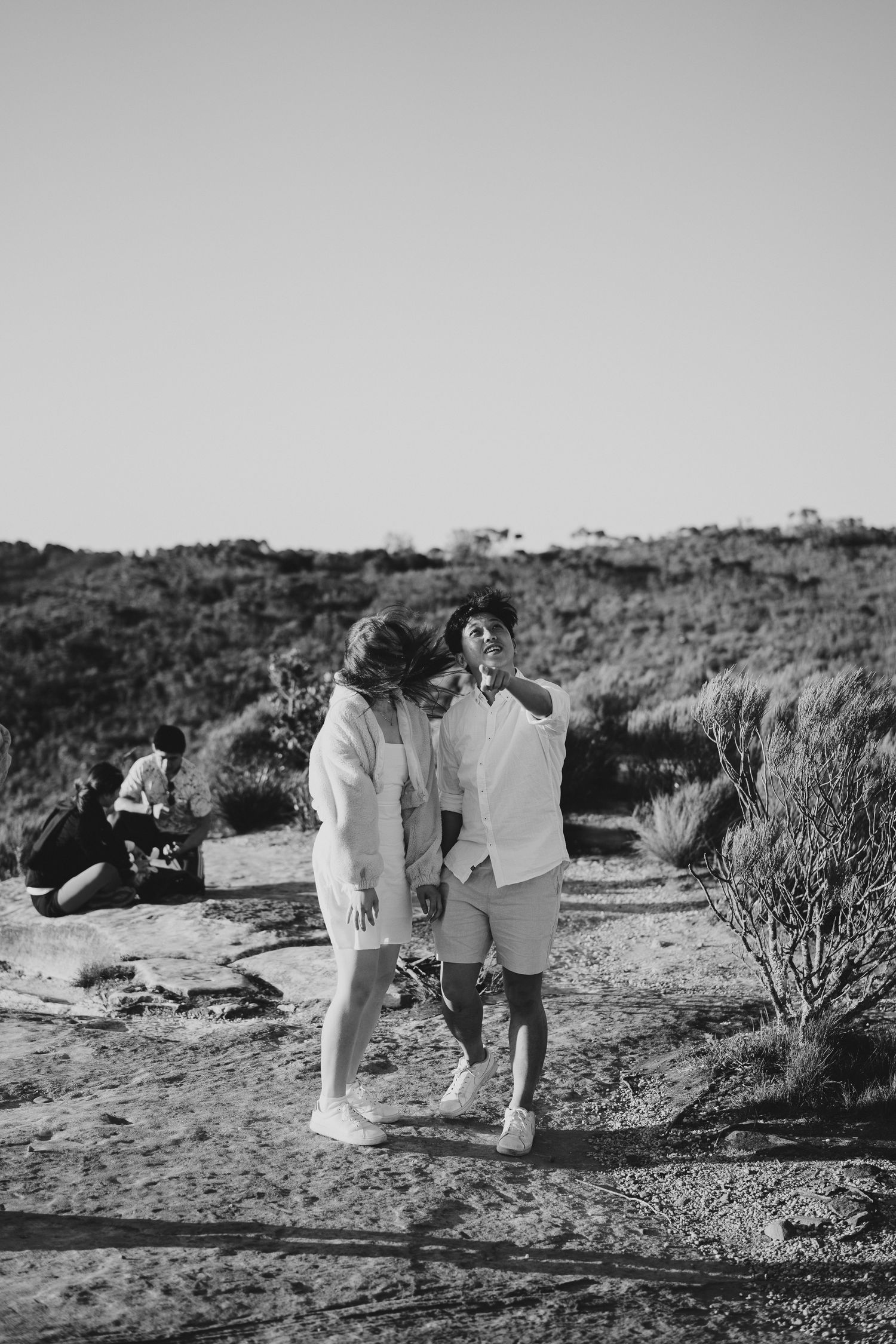 A black and white photo of two people in light clothing sharing an intimate moment on a mountain path.