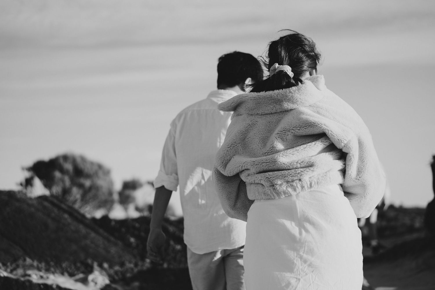 Black and white photo of two people embracing while standing on mountain overlook.
