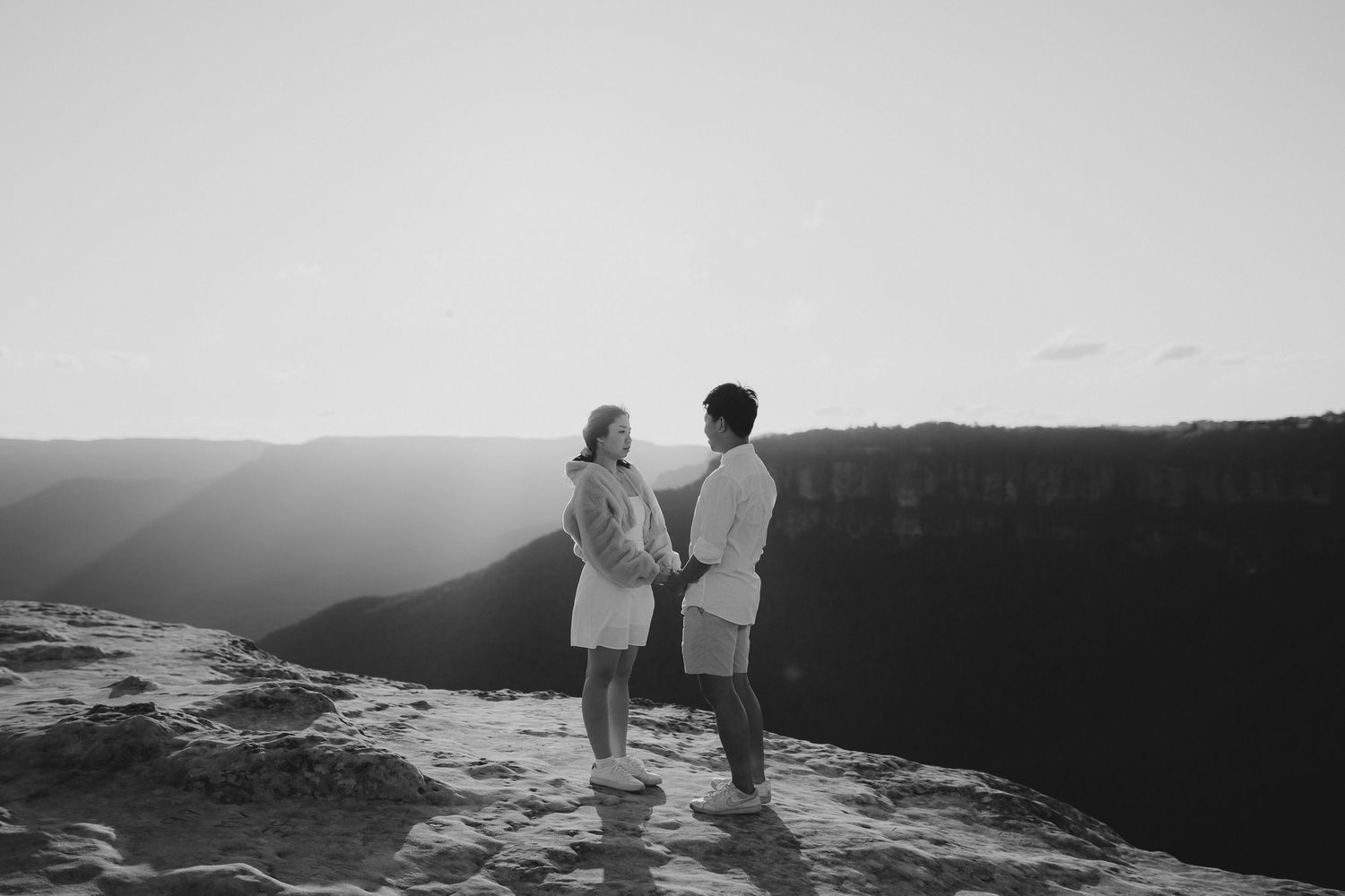 A couple in matching white outfits shares an intimate moment overlooking a dramatic canyon landscape.
