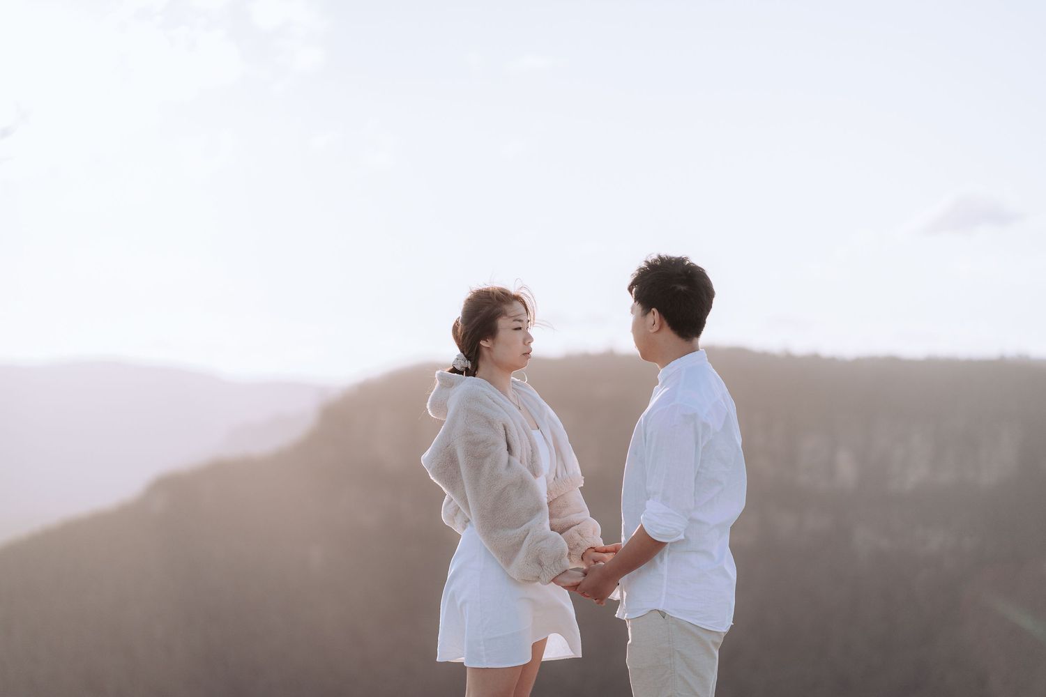 A tender moment between a couple wearing light colored clothing against a misty mountain backdrop.