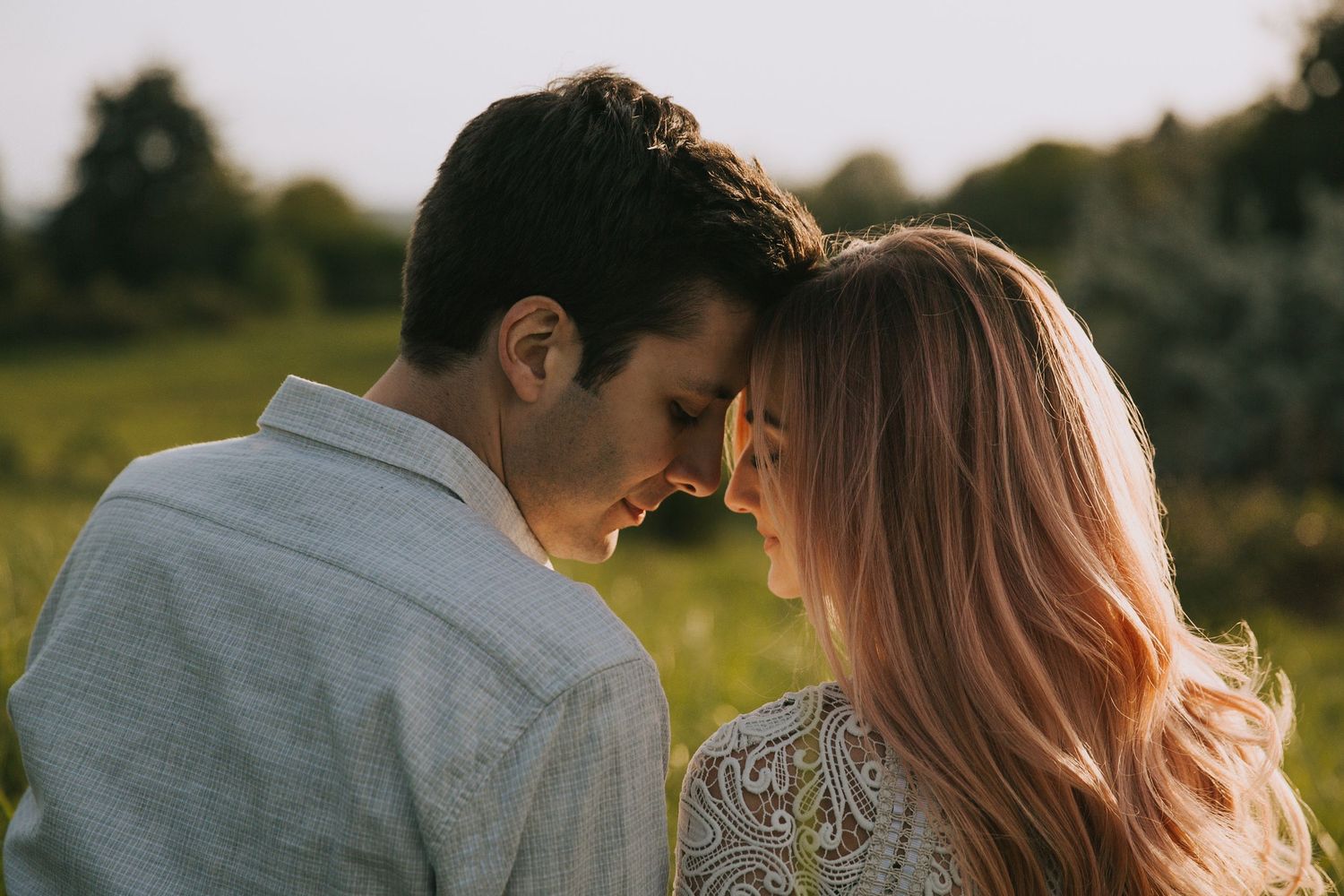 Close romantic couple sharing an intimate moment in a sunlit meadow during golden hour.