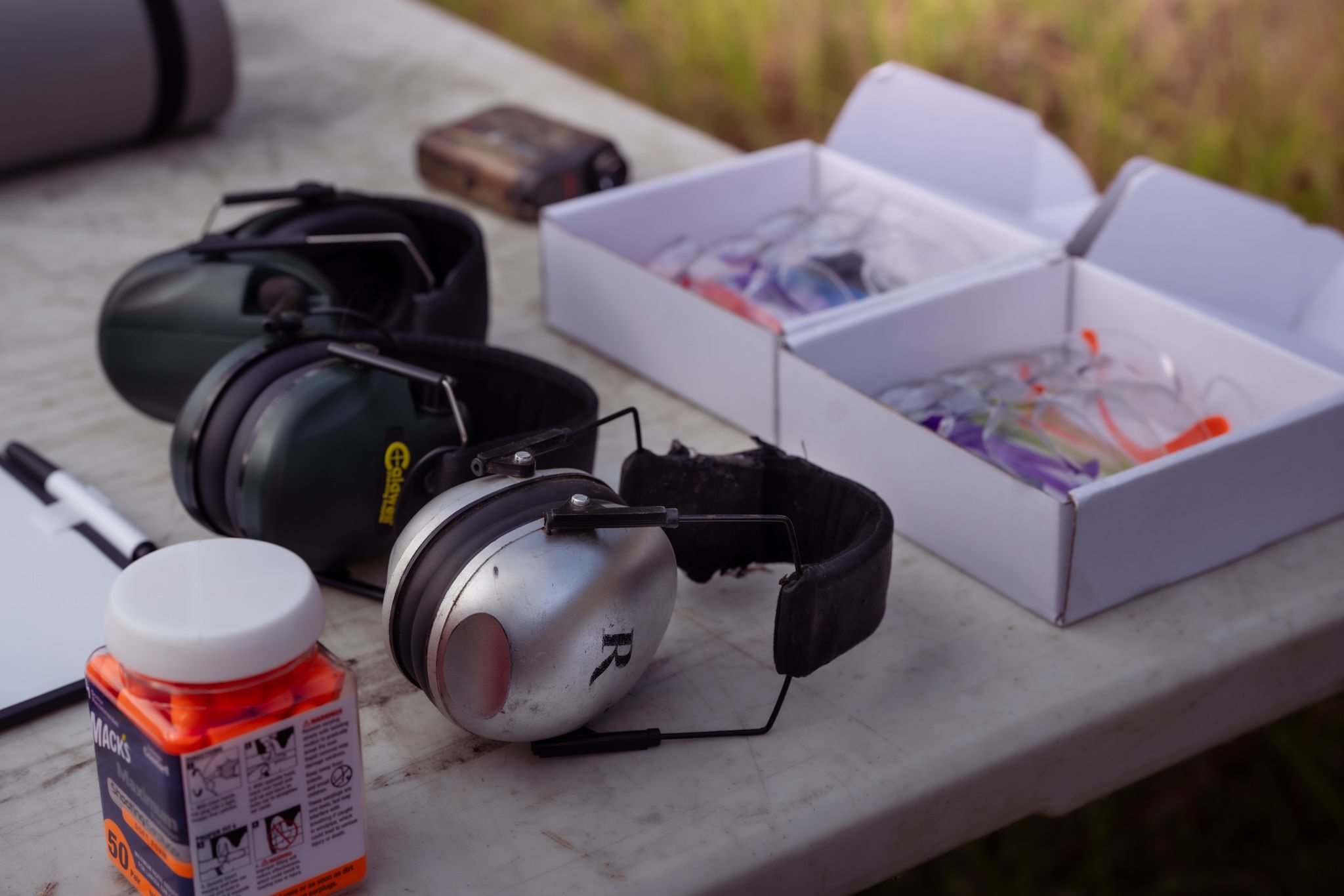 Ear protection headphones and ammunition boxes arranged on a wooden surface outdoors.