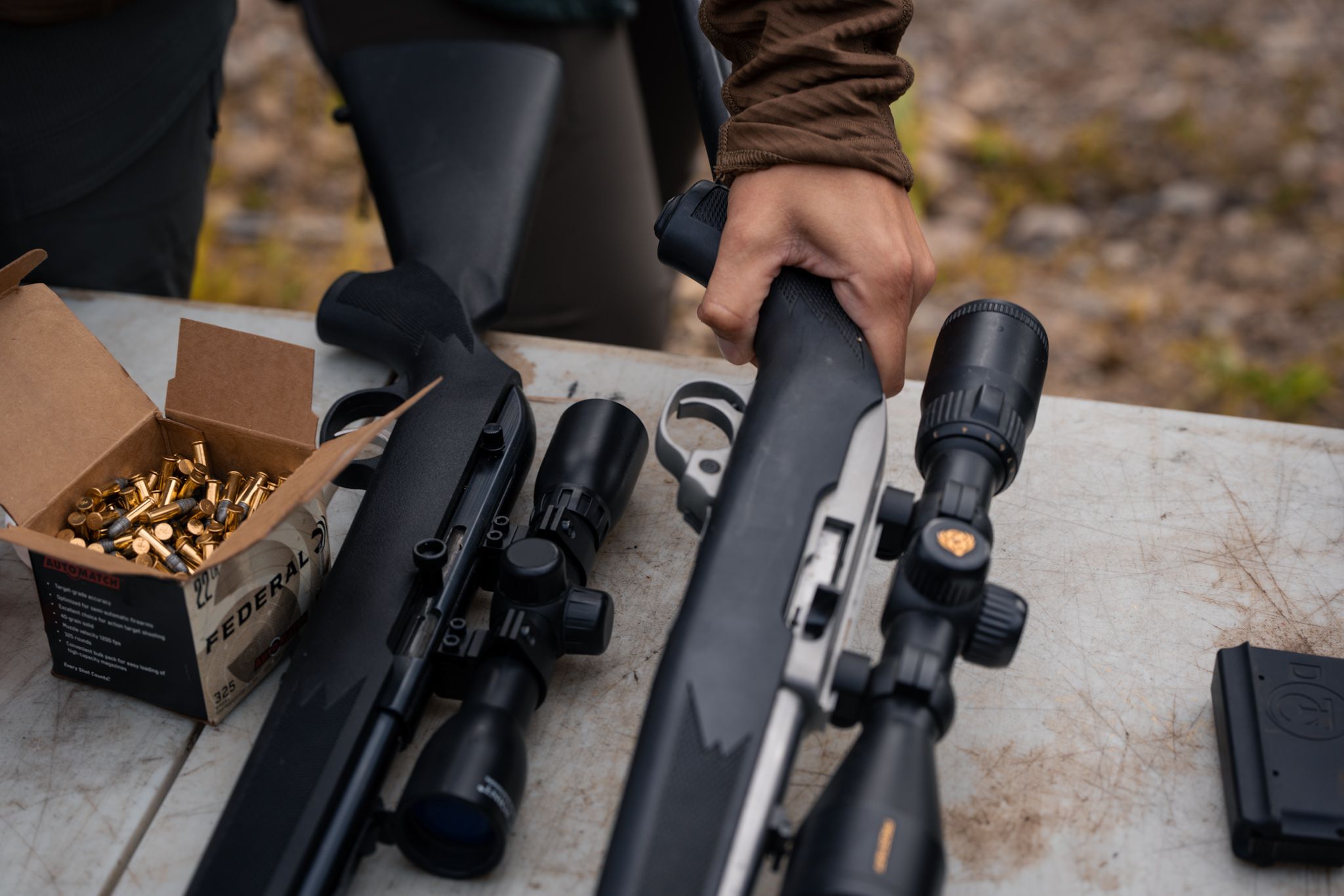 Close up view of firearms and ammunition being loaded on a wooden surface outdoors.