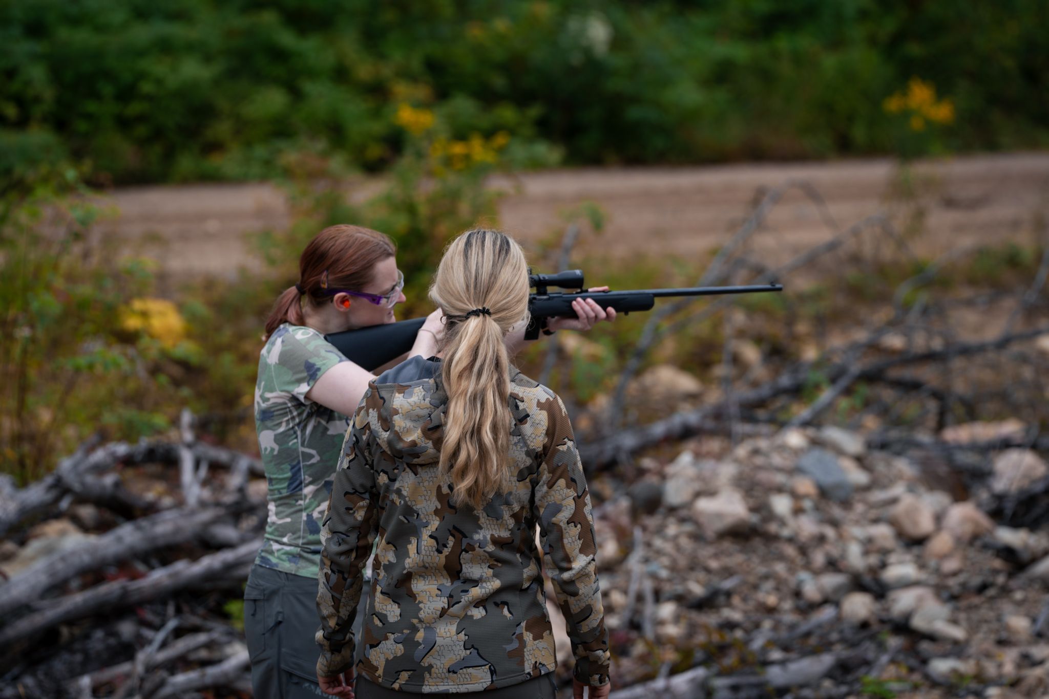 Two hunters in camouflage gear practice shooting at an outdoor target range.