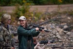 Two people practice proper shooting form and technique with rifles at an outdoor range.