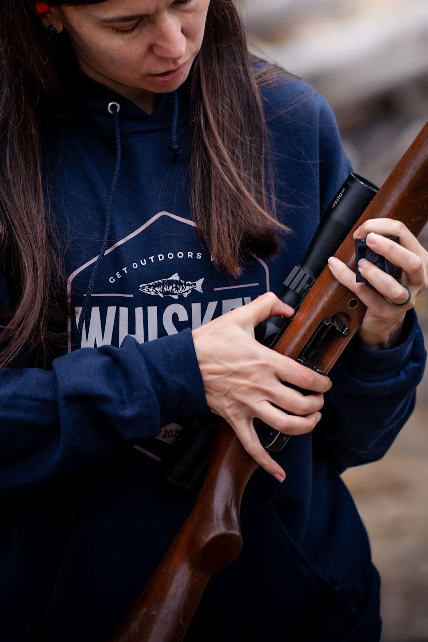 Close-up of person wearing navy blue hoodie with Musky logo examining wooden rifle stock.