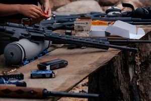 Assorted firearms, ammunition, and shooting accessories laid out on a wooden surface for maintenance and inspection.