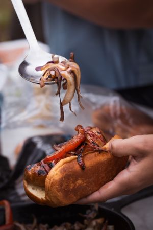A gourmet lobster roll being topped with caramelized onions on a serving plate.