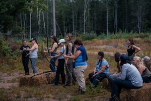 A group of people sitting on a fallen log in a wooded area during an outdoor activity.