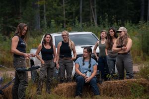 A group in coordinated black tops and cargo pants poses casually on hay bales in front of a parked vehicle.
