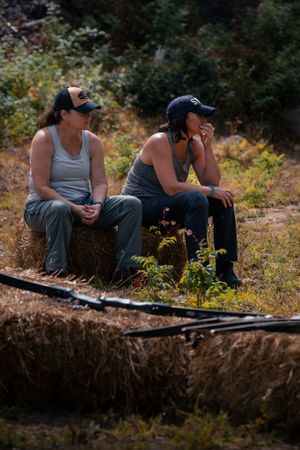 Two mountain bikers taking a break while sitting on a dirt trail surrounded by autumn foliage.