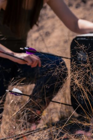 A person sitting on dry ground holding a purple pen against a backdrop of dried grass stems and brush.