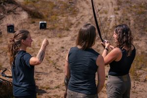 Three people practicing archery outdoors at a shooting range with a rocky backdrop.