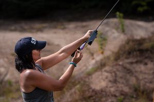 A rock climber grips a belay rope while wearing a blue baseball cap and tank top during an outdoor climbing session.