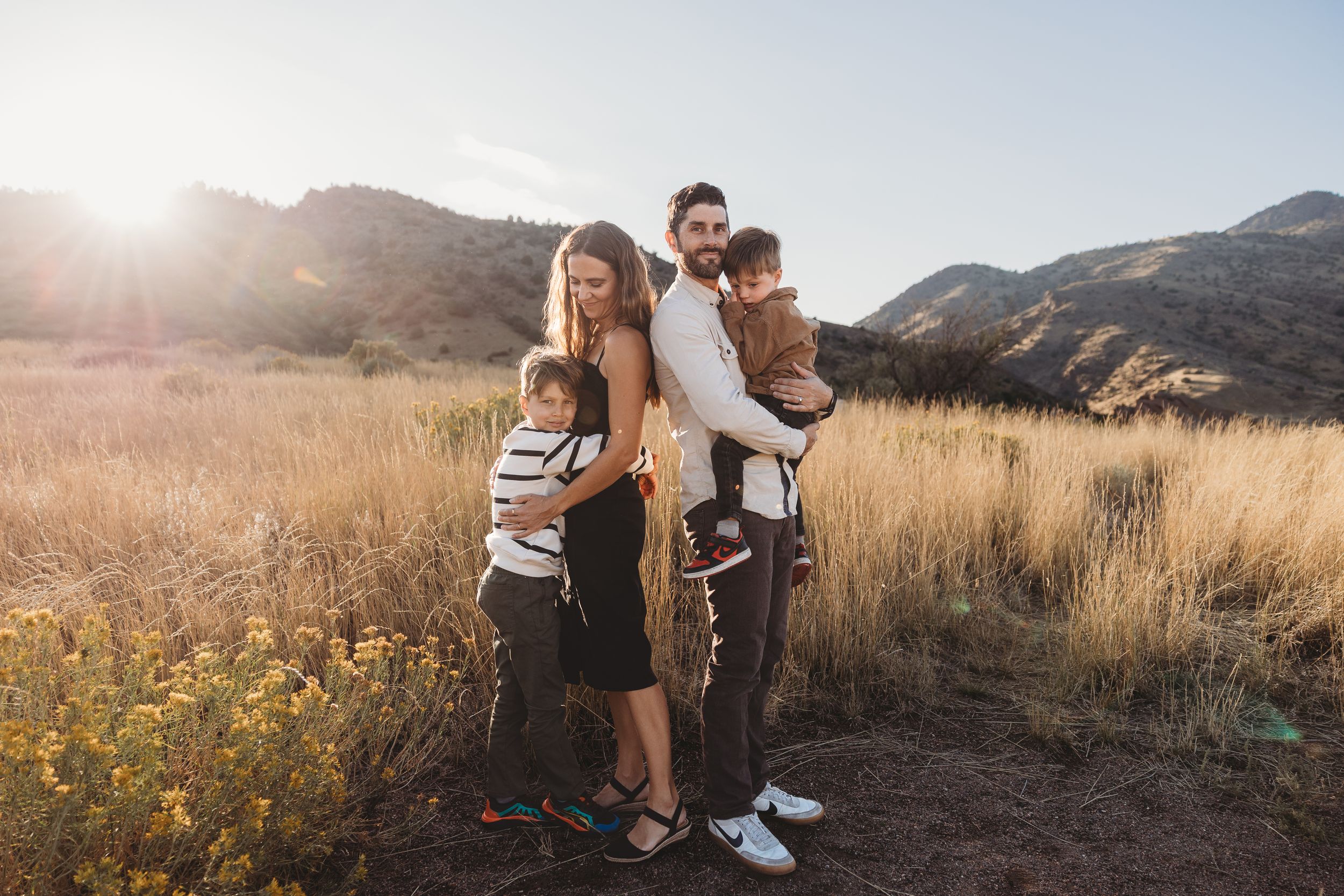 Young family of four posing together at sunset with mountains in background, set in Morrison and Golden Colorado.