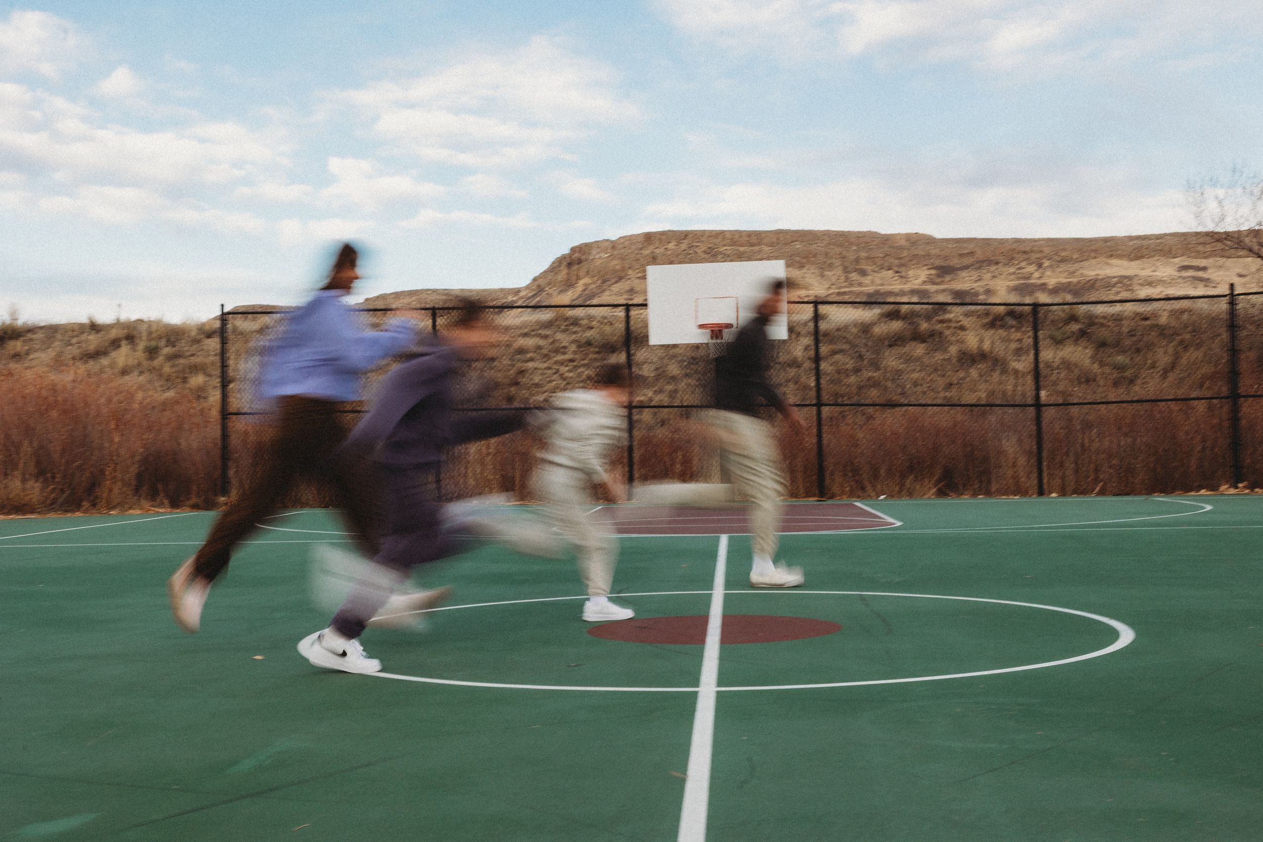 Motion blur of people playing basketball on an outdoor court with desert landscape background.